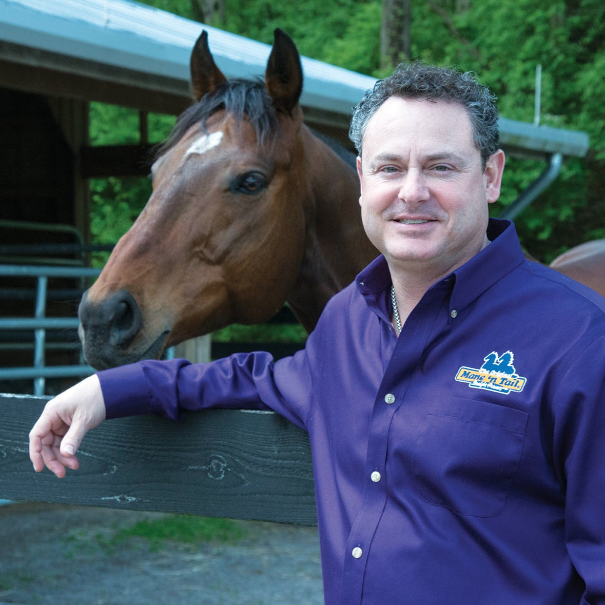 Man in a blue jacket standing next to a horse in an outdoor setting