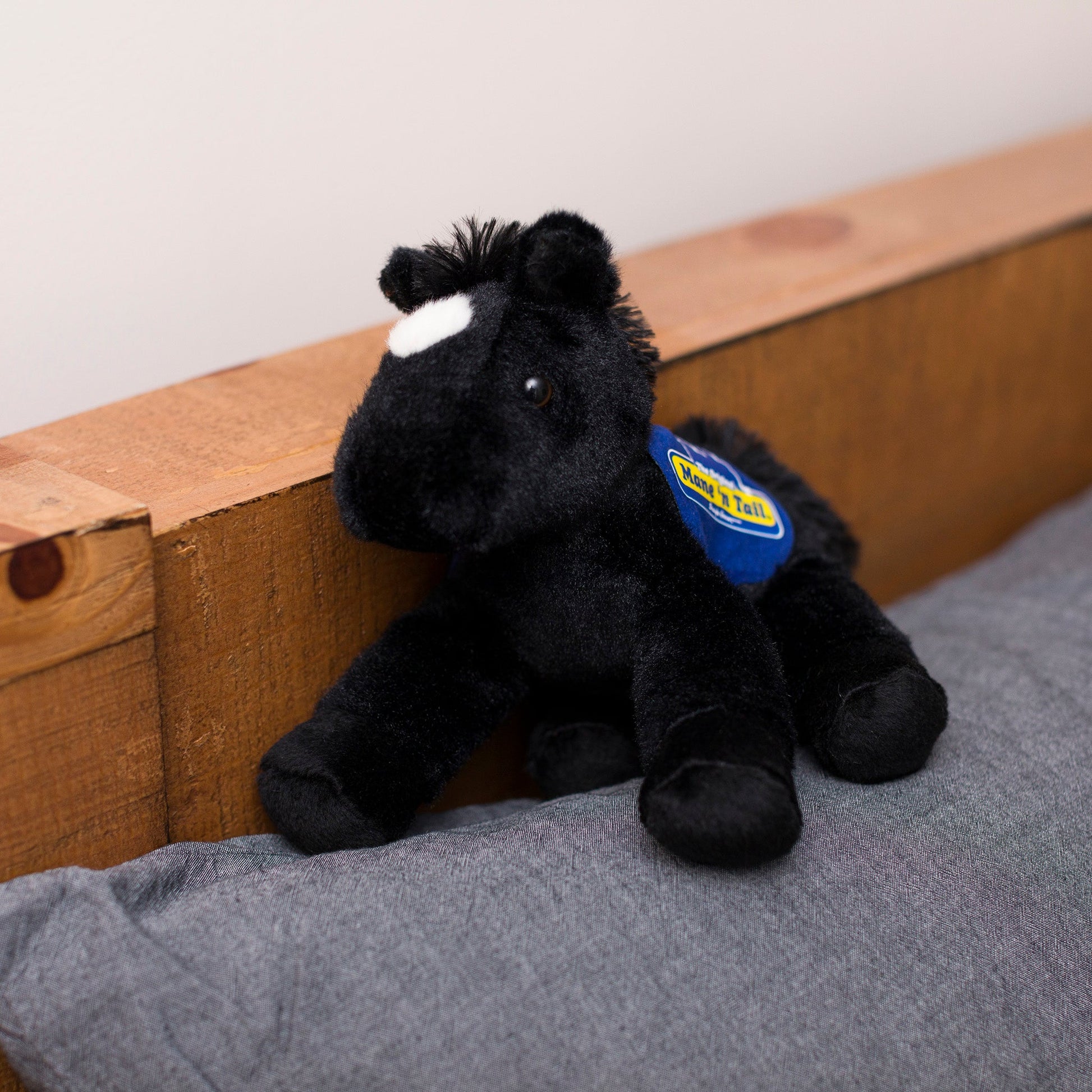 Small Beau Horse horse stuffed animal wearing a royal blue branded mane 'n tail saddle. Standing on a cushion
