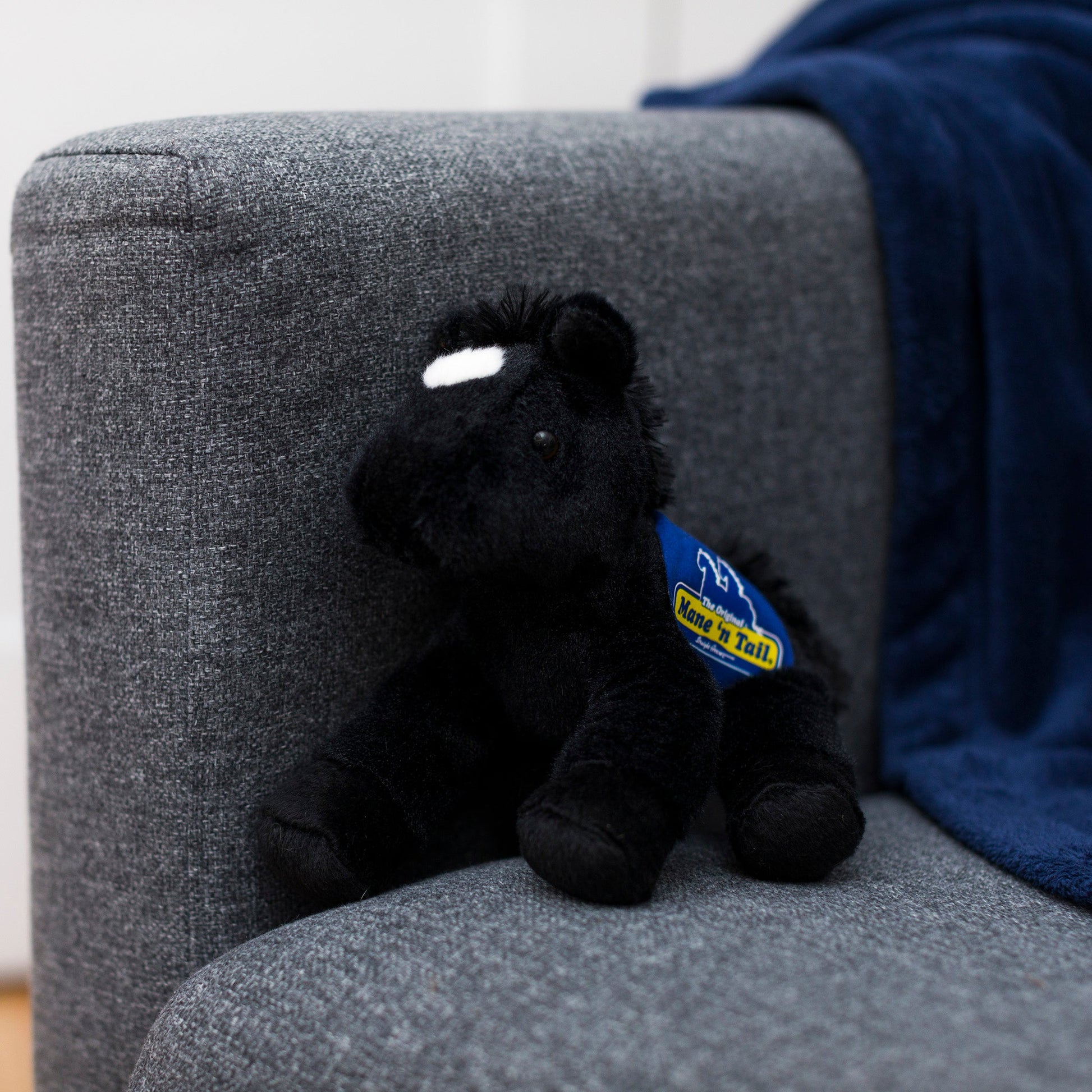 Small Beau Horse horse stuffed animal wearing a royal blue branded mane 'n tail saddle. Standing on a couch