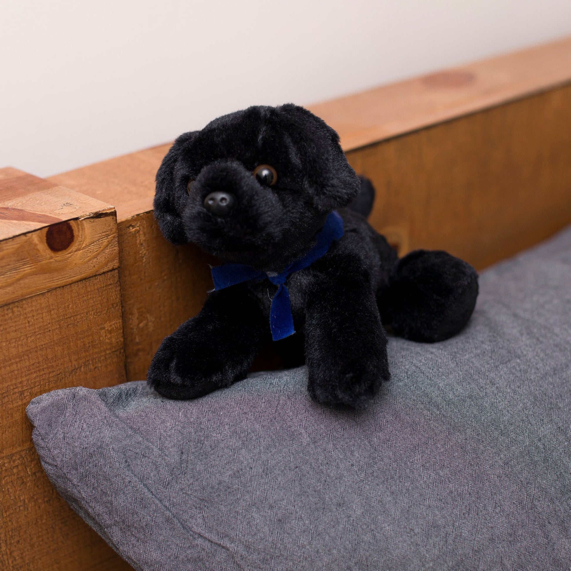 Small Boston Terrier dog stuffed animal wearing a royal blue branded mane 'n tail bandana. Standing on a cushion