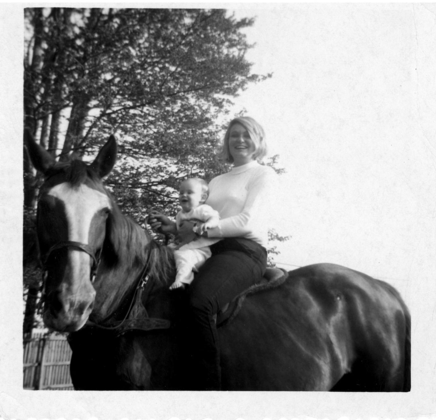 A black and white picture of Bonnie, Devon's mother, holding a baby Devon while on horseback. 