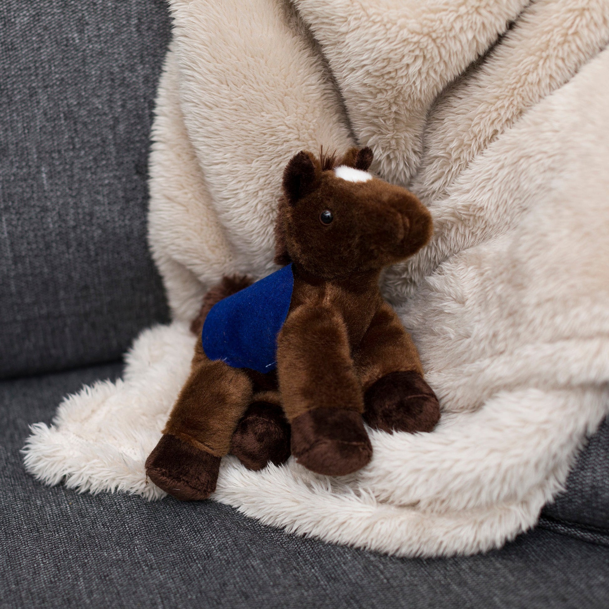 Small Chestnut horse stuffed animal wearing a royal blue branded mane 'n tail saddle. Standing on a blanket
