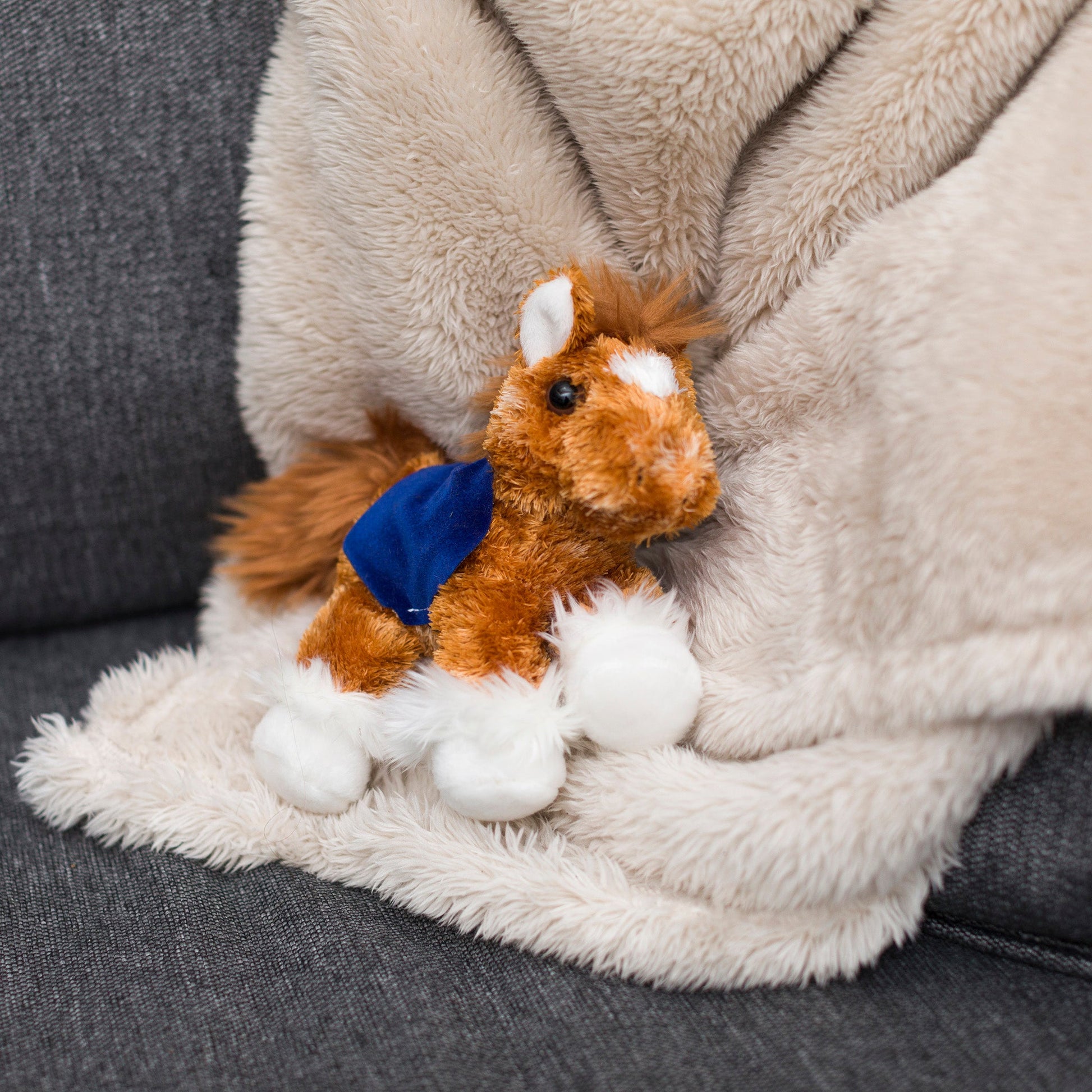 Small orange Clydes horse stuffed animal wearing a royal blue branded mane 'n tail saddle. Standing on a blanket