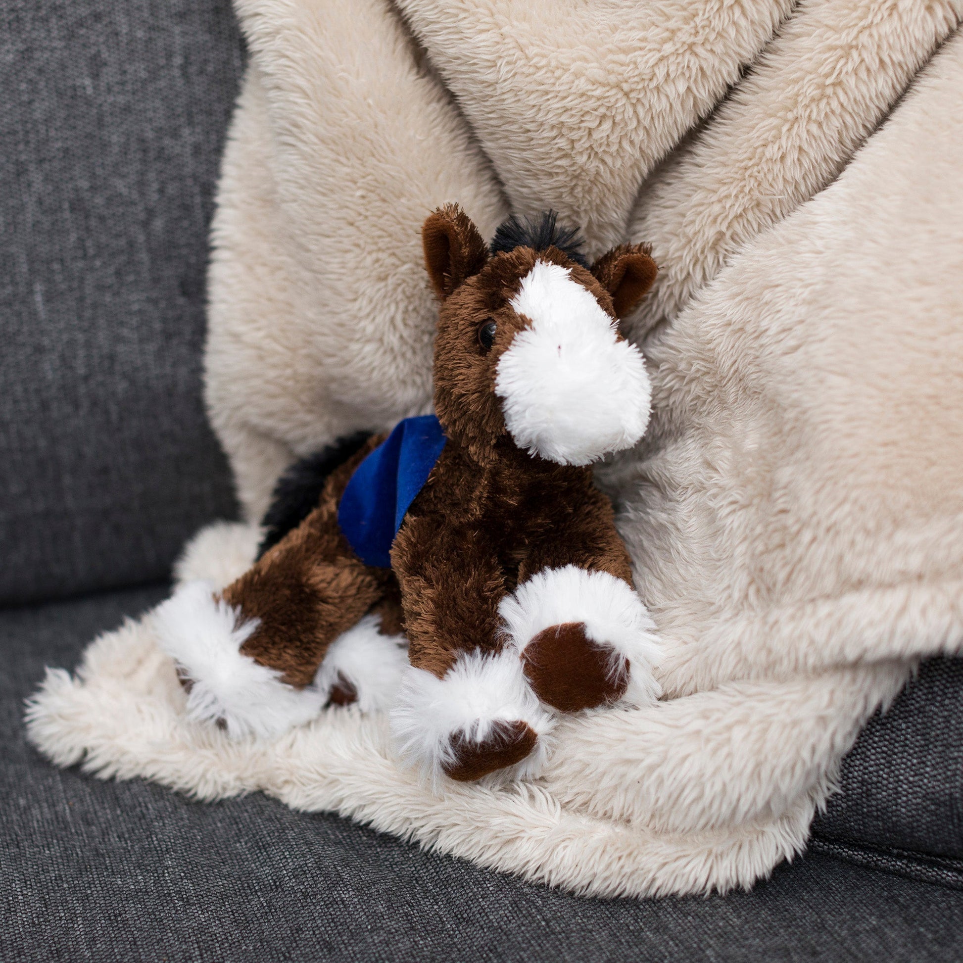 Small brown Clydes horse stuffed animal wearing a royal blue branded mane 'n tail saddle. Standing on a blanket