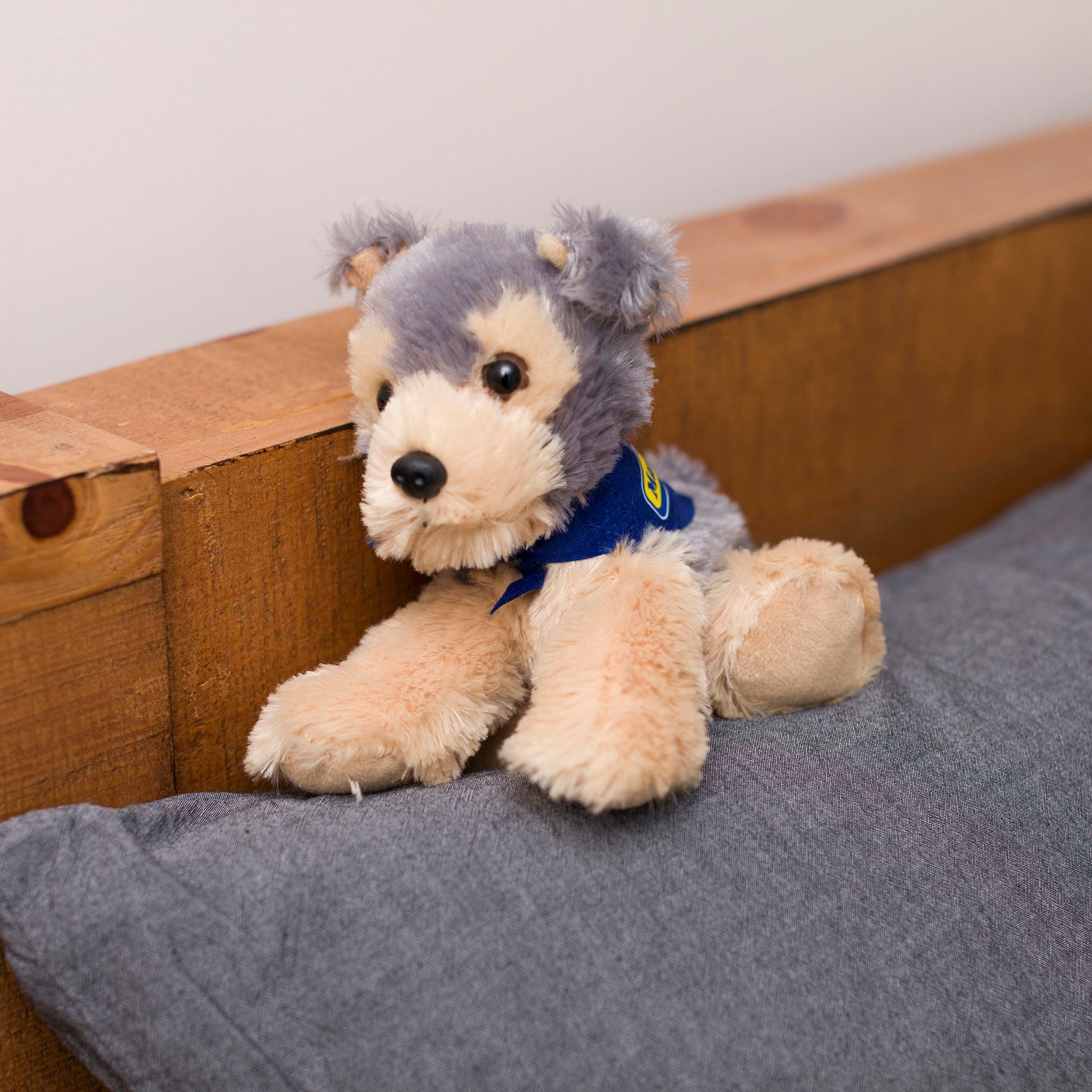 Small Yorkshire Terrier dog stuffed animal wearing a royal blue branded mane 'n tail bandana. Standing on a cushion