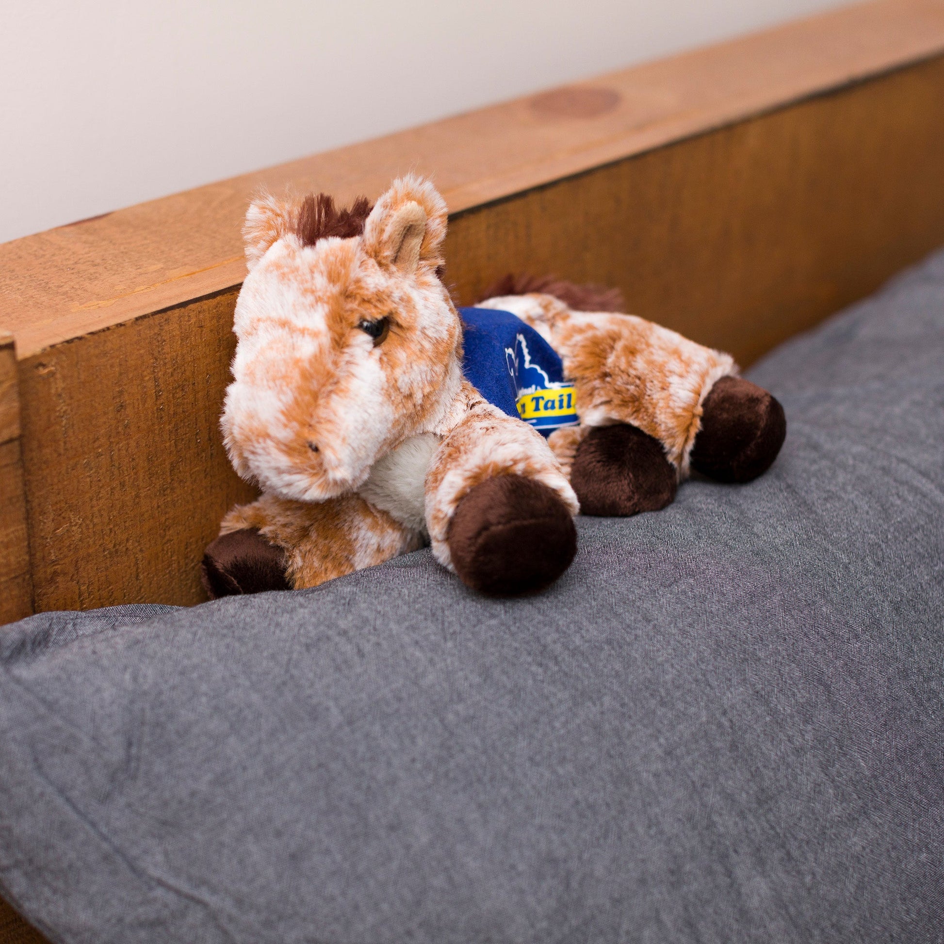 Small Mocha horse stuffed animal wearing a royal blue branded mane 'n tail saddle. Standing on a cushion