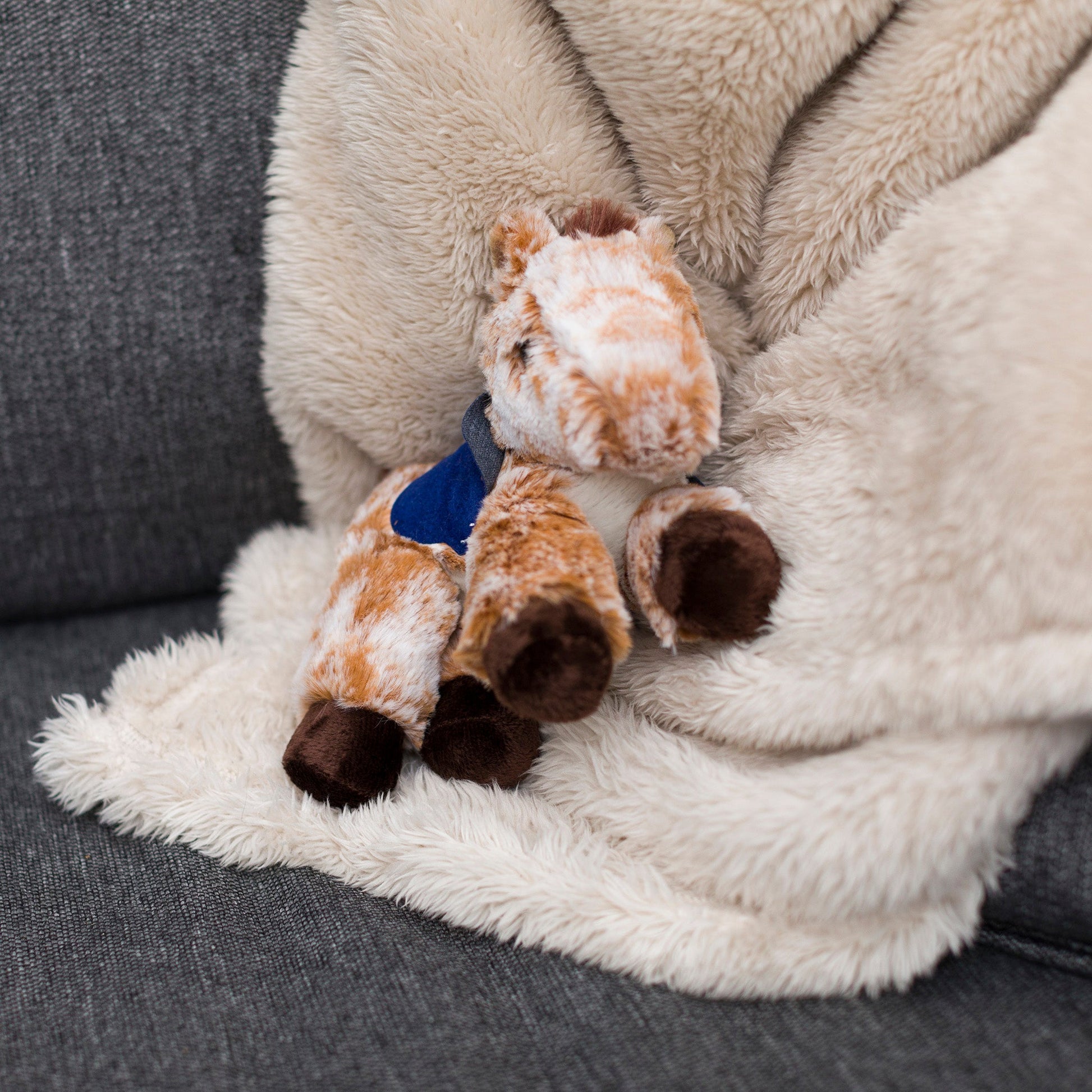 Small Mocha horse stuffed animal wearing a royal blue branded mane 'n tail saddle. Standing on a blanket