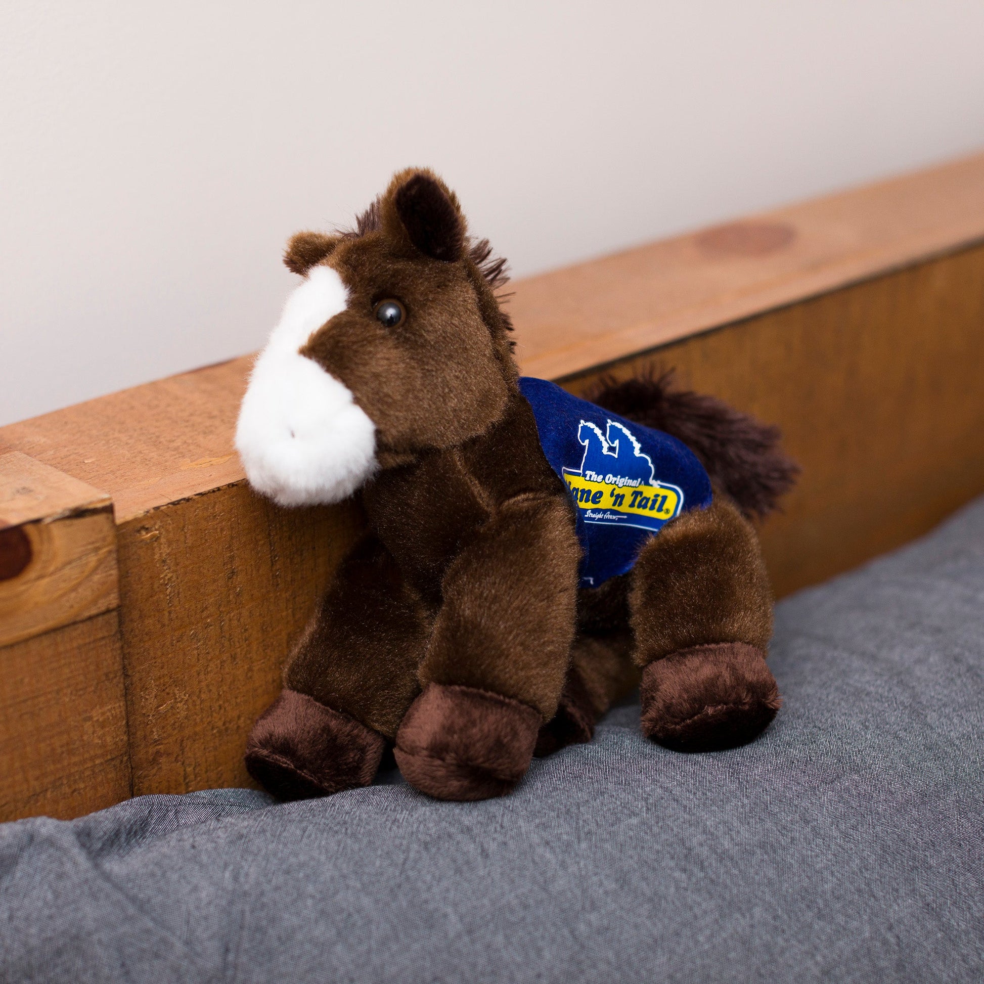 Small Paint horse stuffed animal wearing a royal blue branded mane 'n tail saddle. Standing on the cushion