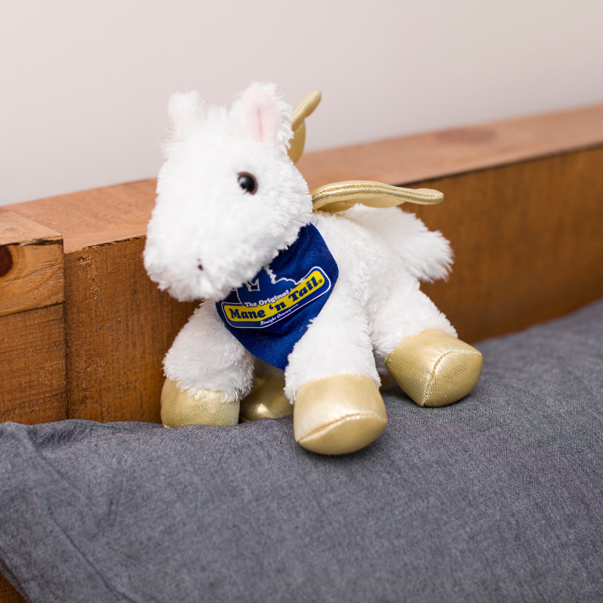 Small Pegasus horse stuffed animal wearing a royal blue branded mane 'n tail bandana. Standing on a cushion