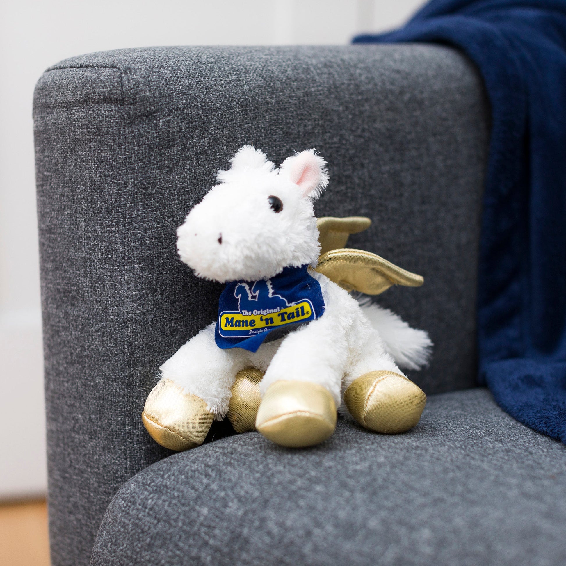 Small Pegasus horse stuffed animal wearing a royal blue branded mane 'n tail bandana. Standing on a couch