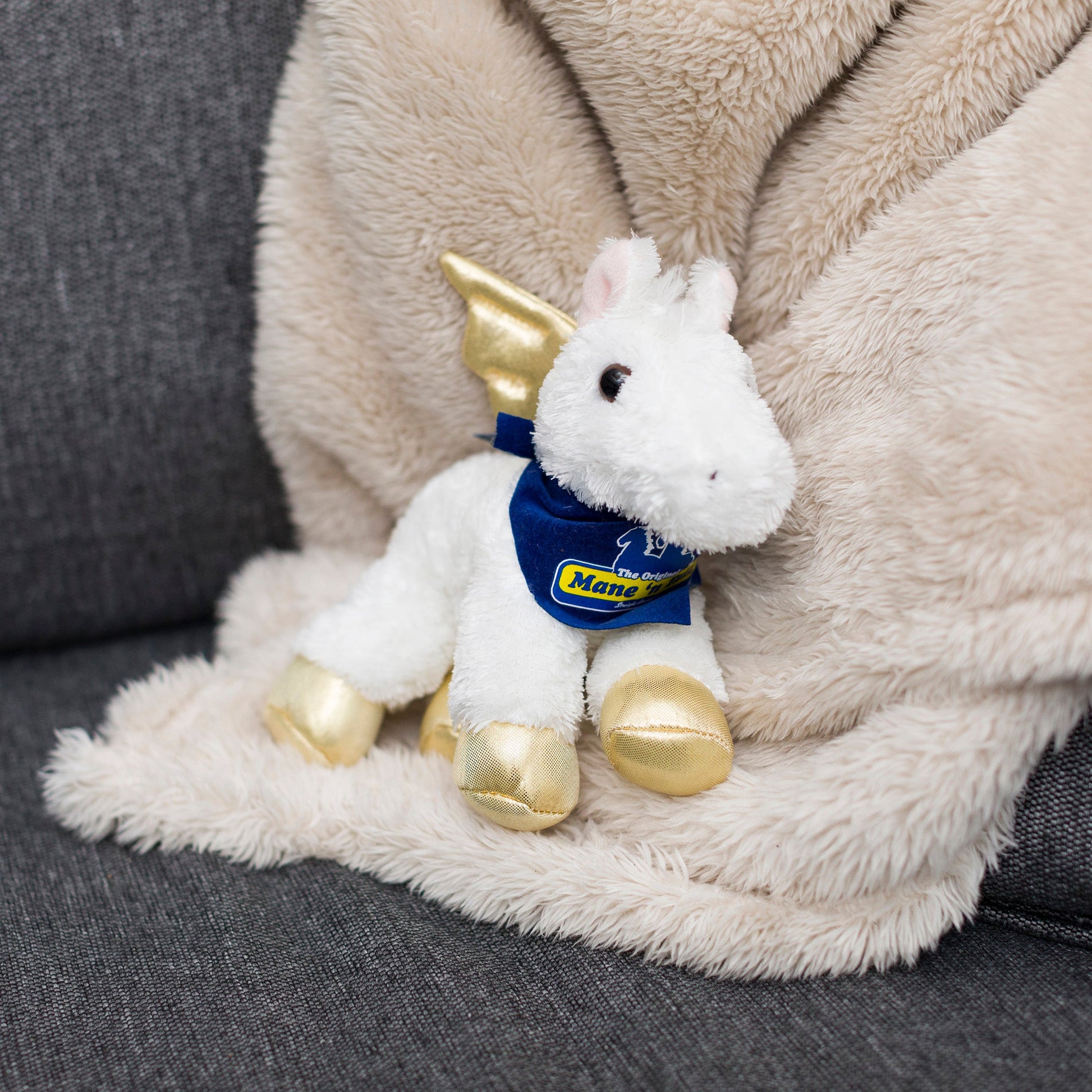 Small Pegasus horse stuffed animal wearing a royal blue branded mane 'n tail bandana. Standing on a blanket