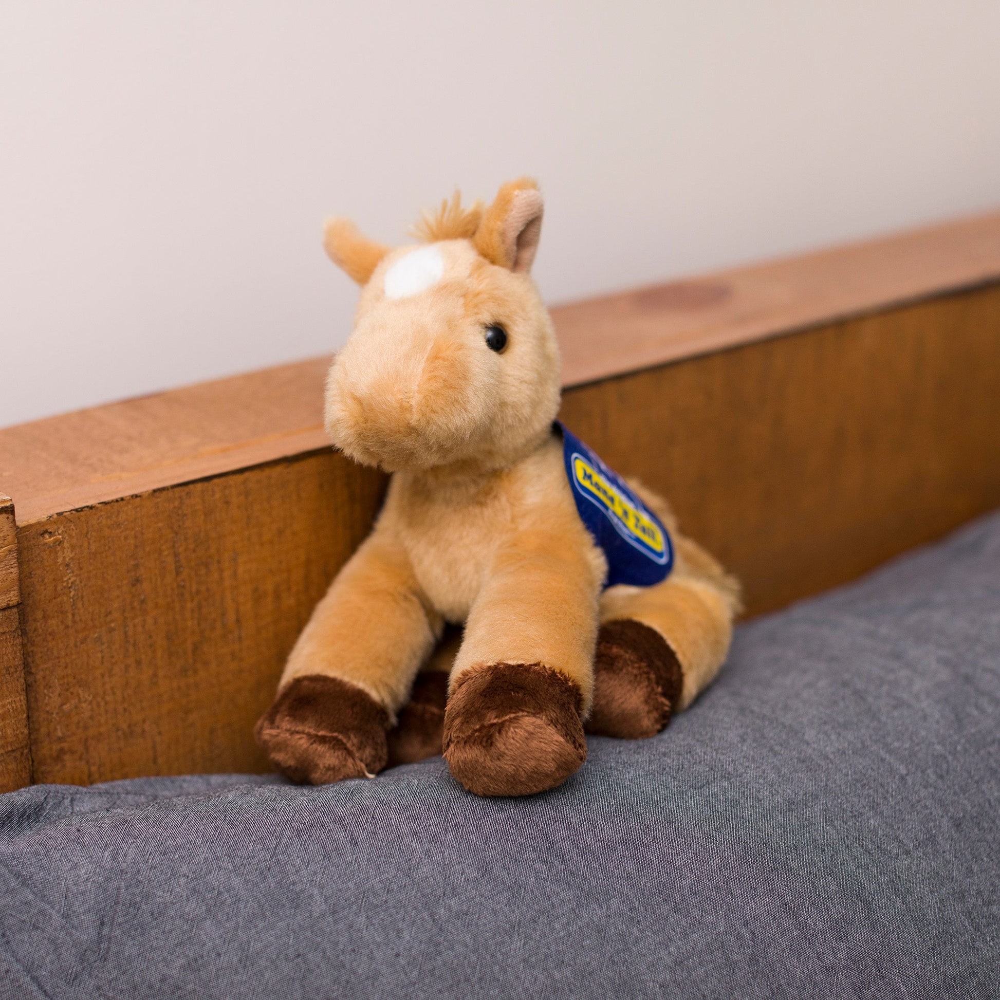 Small Prancer Horse horse stuffed animal wearing a royal blue branded mane 'n tail saddle. Standing on a cushion