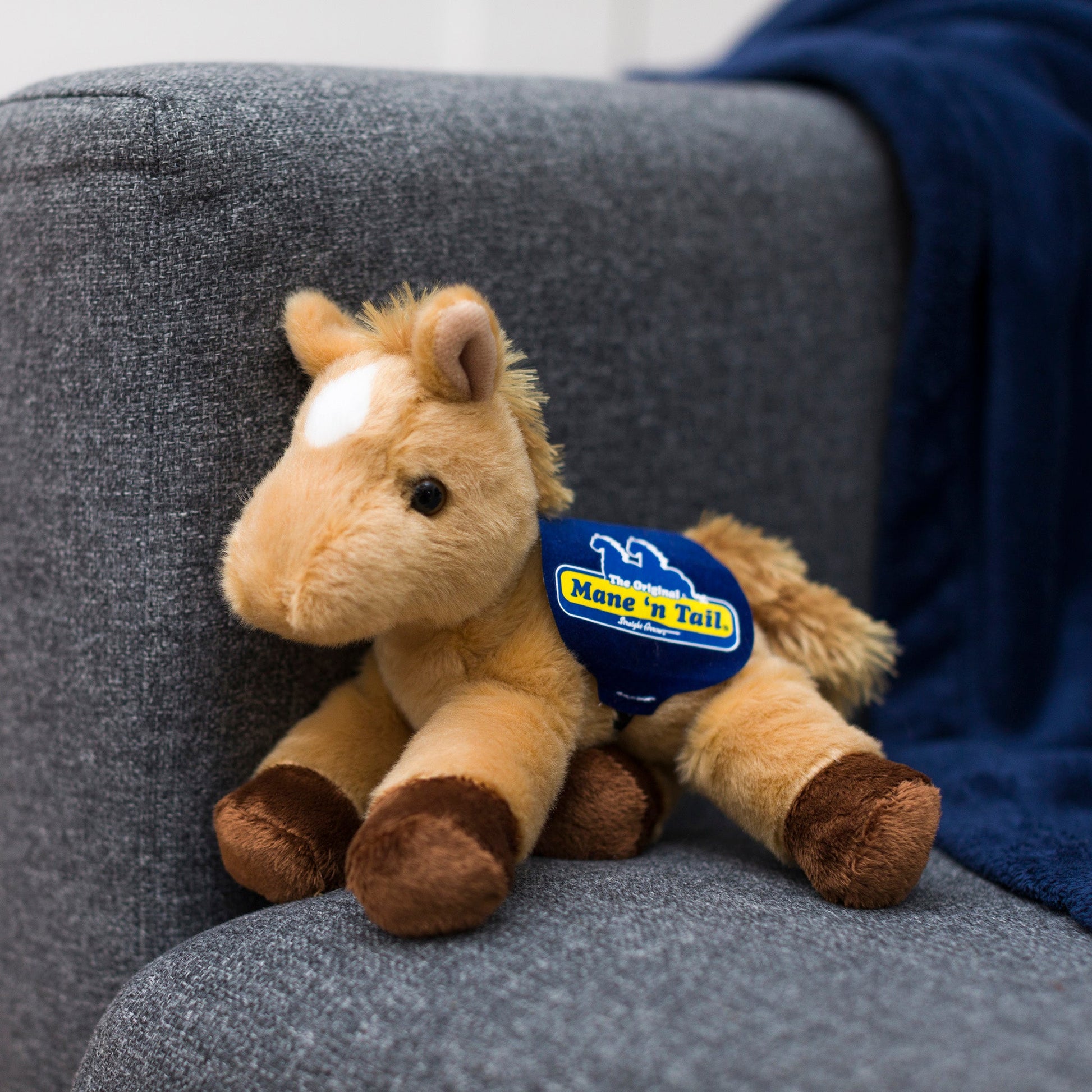 Small Prancer Horse horse stuffed animal wearing a royal blue branded mane 'n tail saddle. Standing on a couch