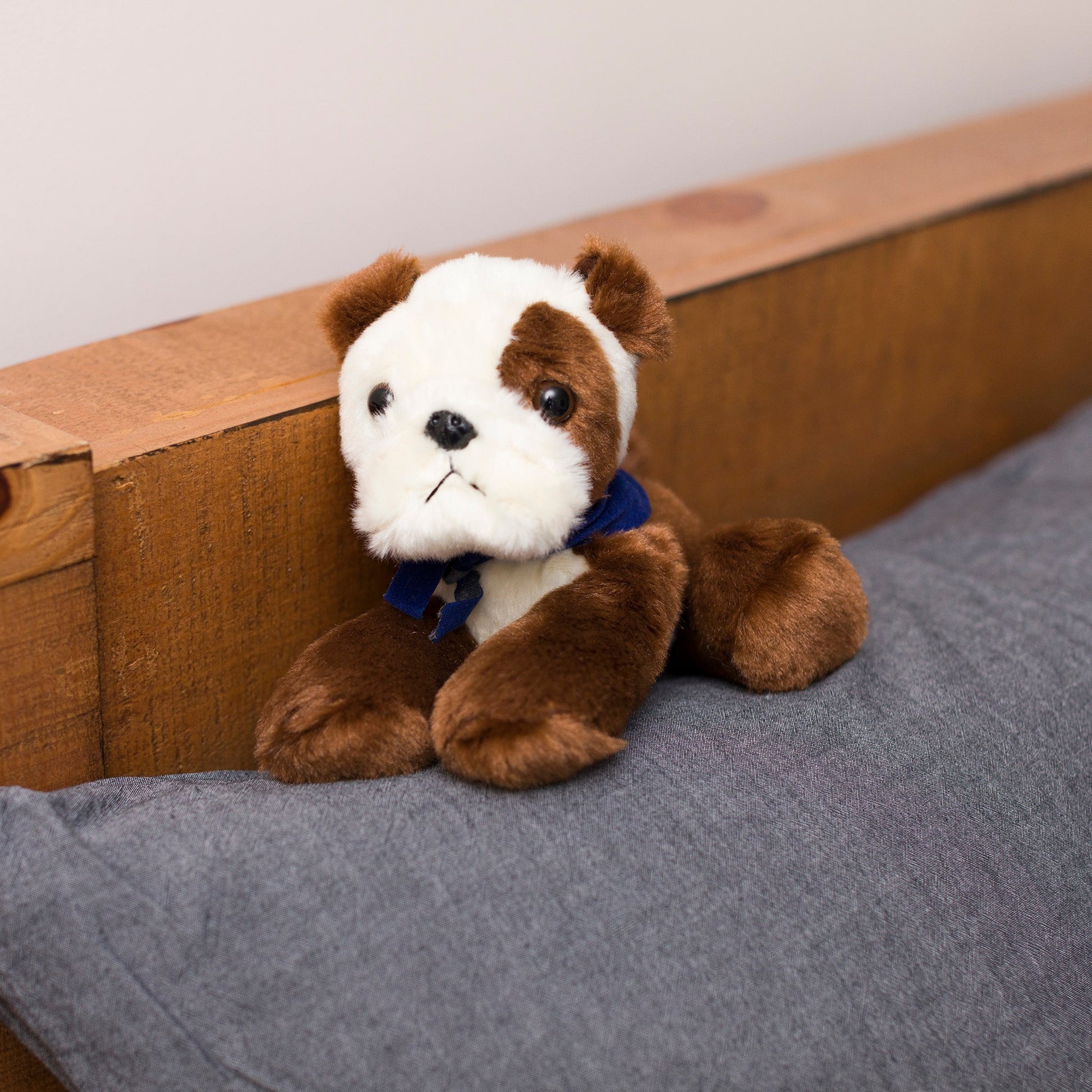 Small Bulldog stuffed animal wearing a royal blue branded mane 'n tail bandana. Standing on a cushion