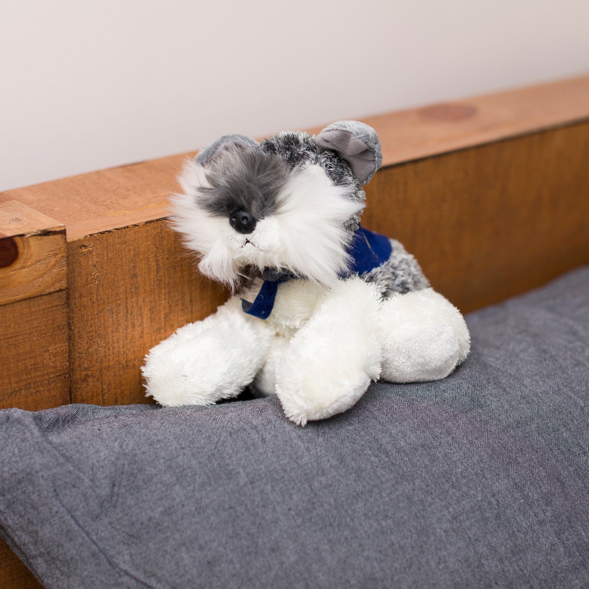 Small Stein Schnauzer stuffed animal wearing a royal blue branded mane 'n tail bandana. Standing on a cushion.